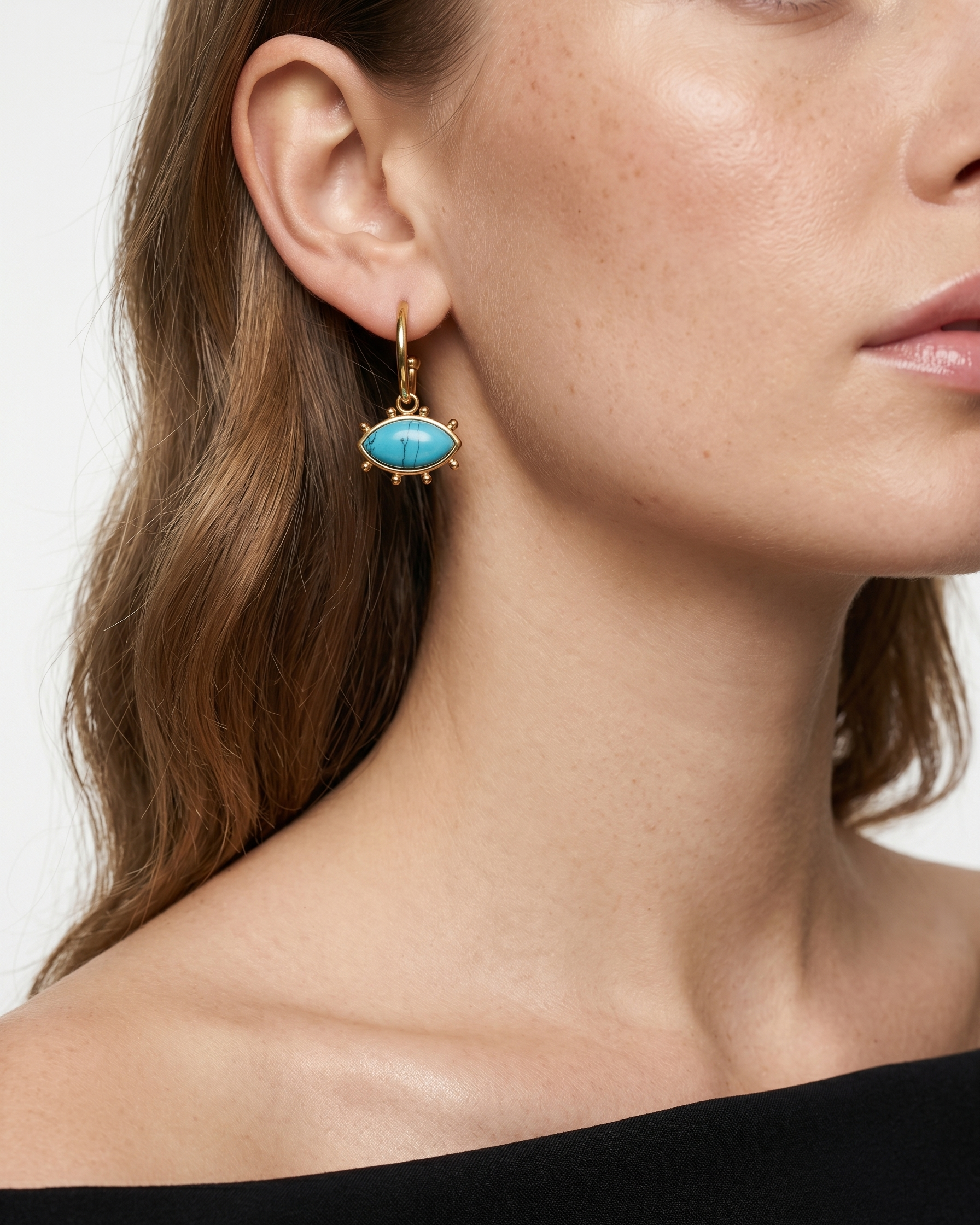 Close-up of a woman wearing a turquoise earring with gold setting.