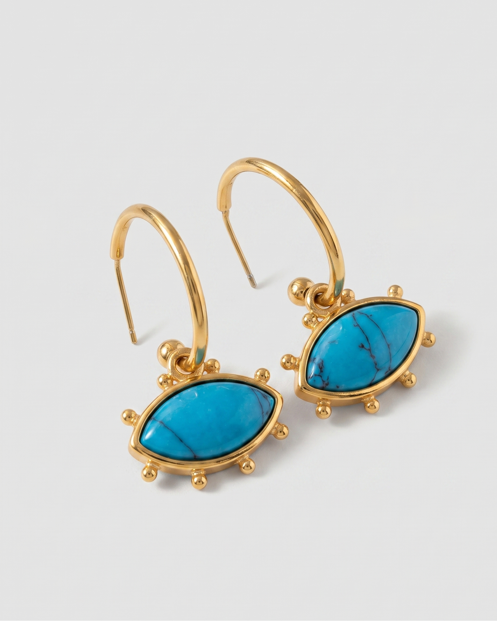 Gold earrings with turquoise stones on a light gray background