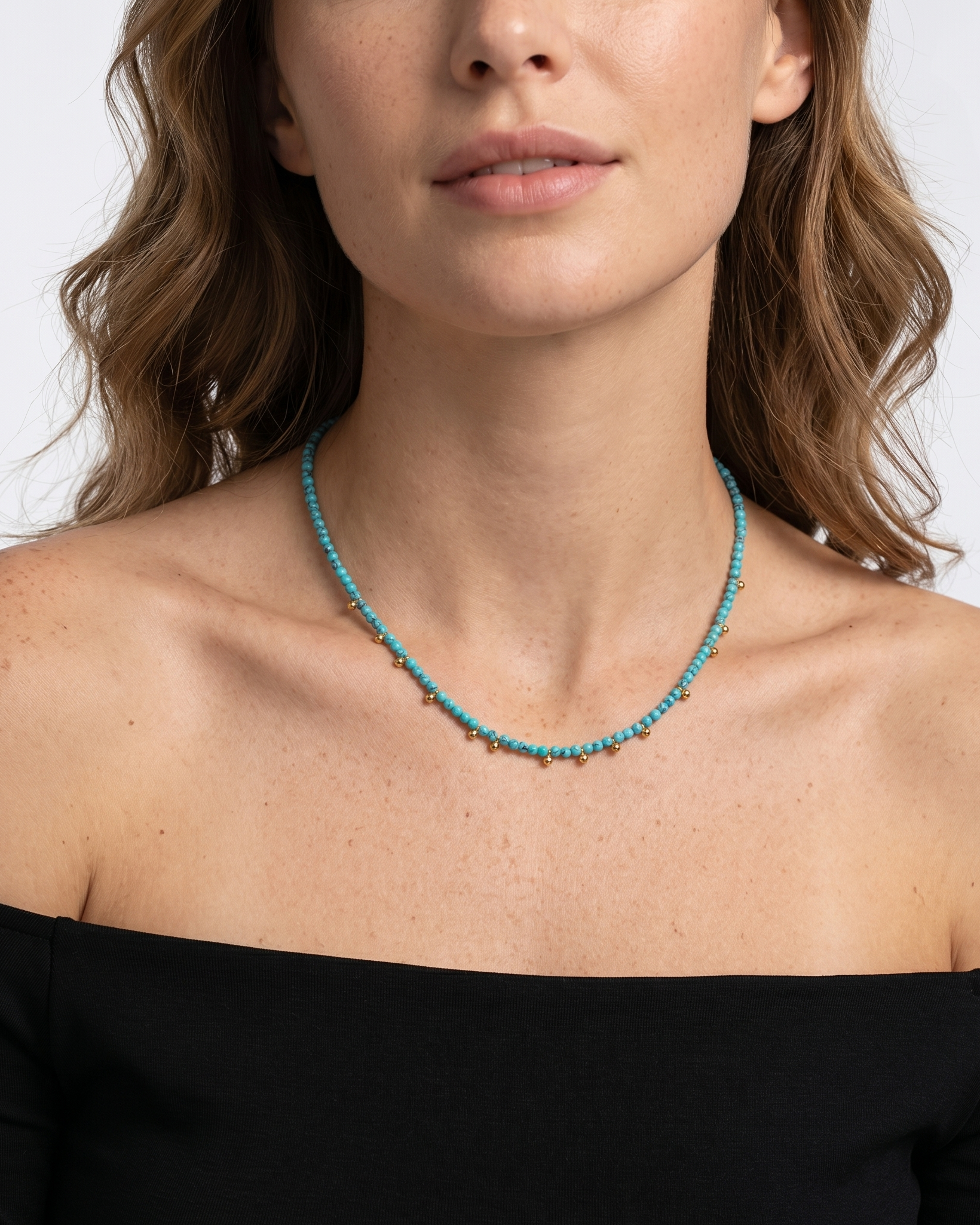 Woman wearing a turquoise beaded necklace against a plain background