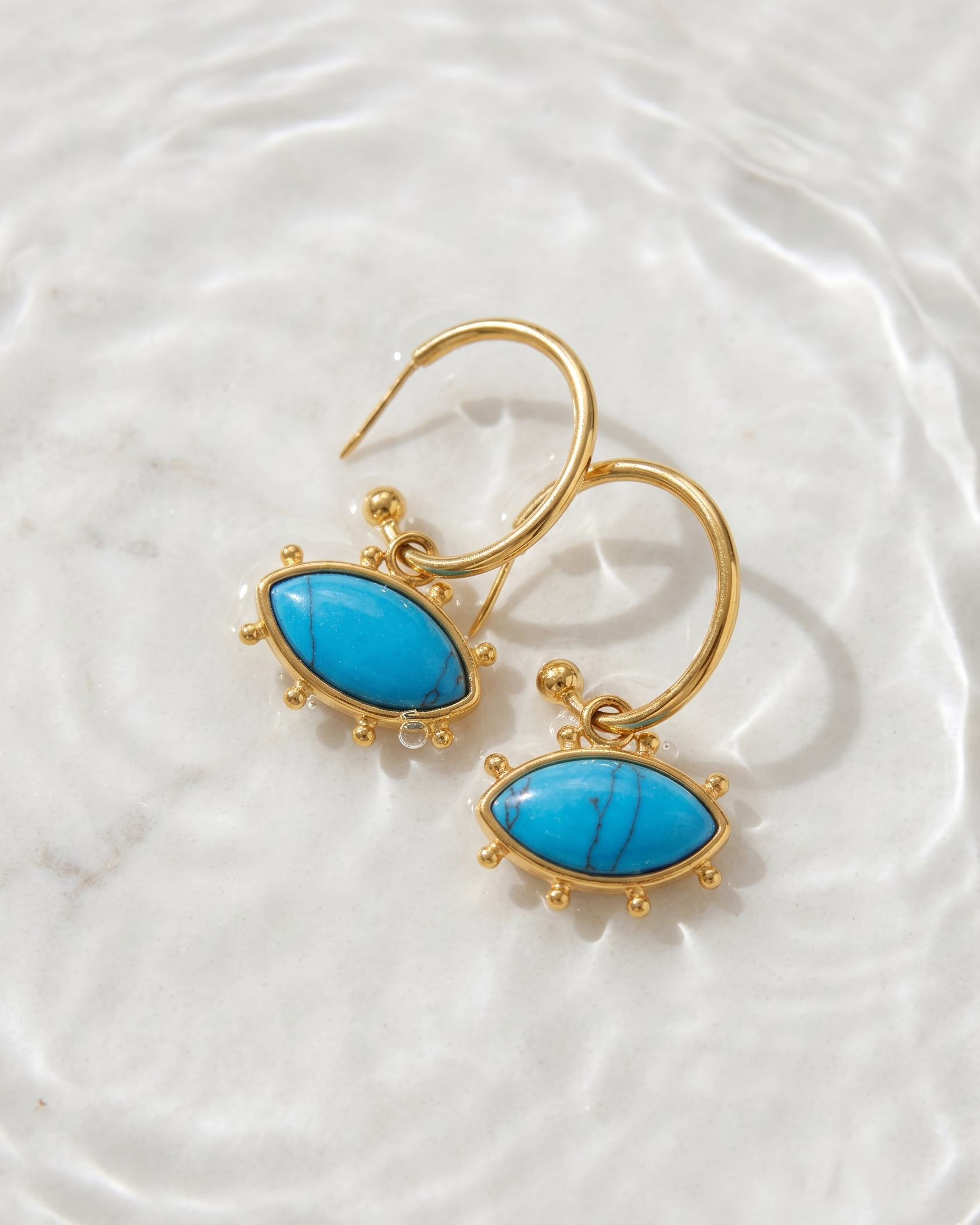 Gold earrings with turquoise stones on a white textured background