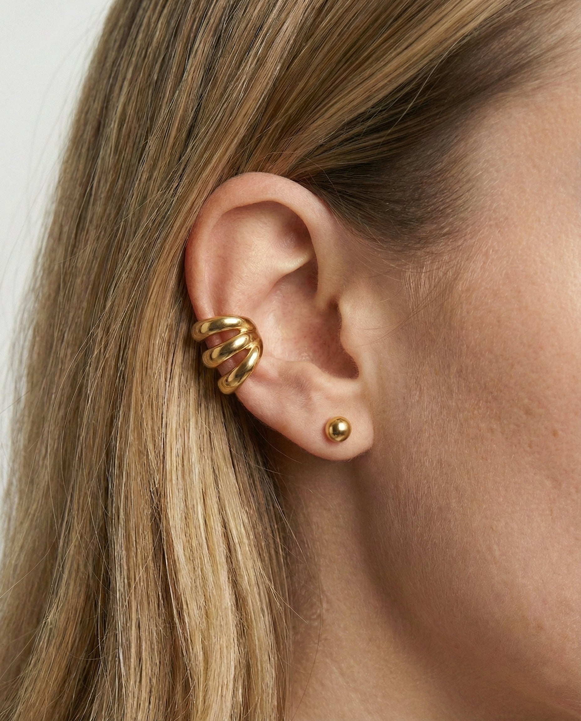 Close-up of an ear wearing gold earrings with a plain background