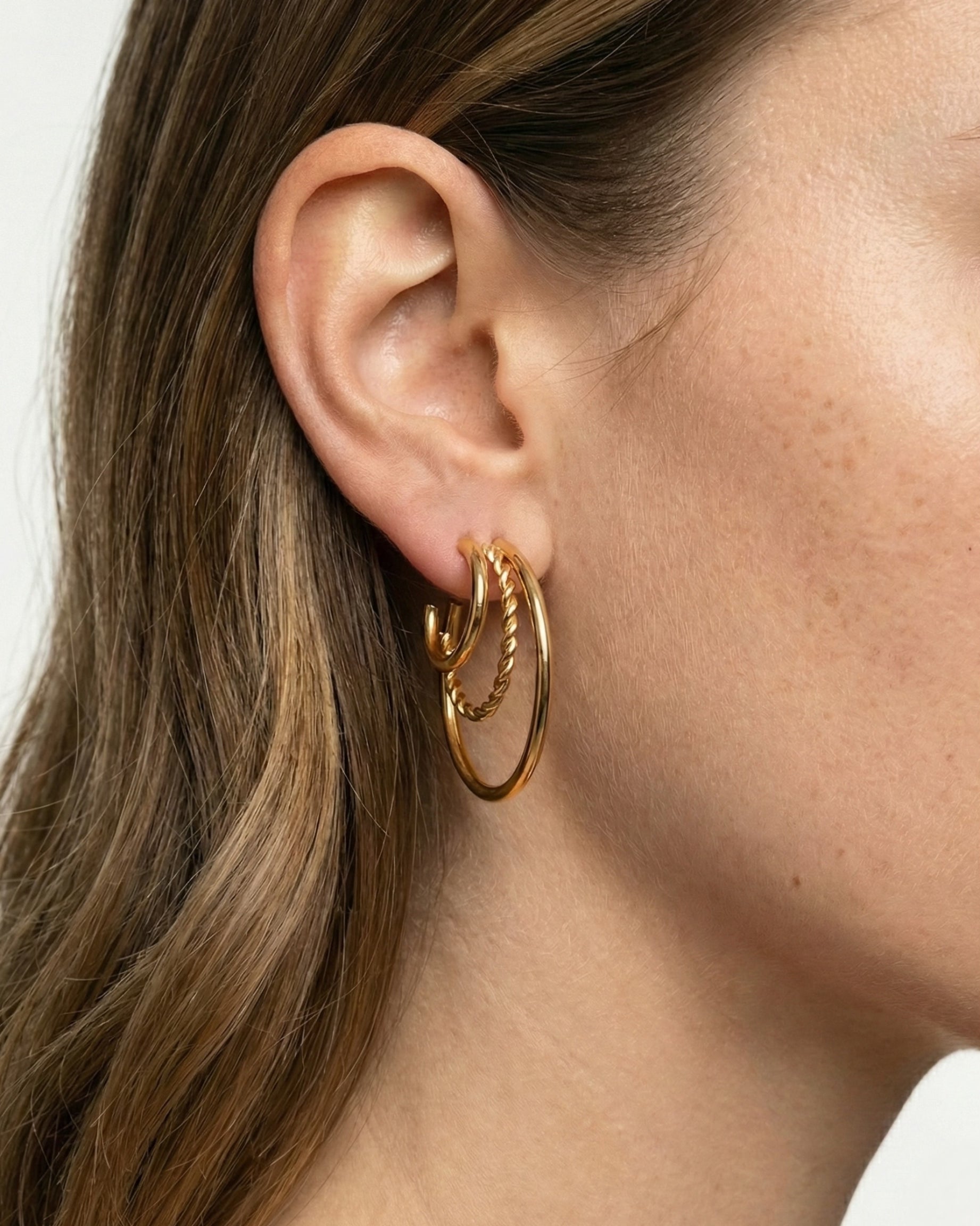 Close-up of a person wearing gold hoop earrings with a neutral background