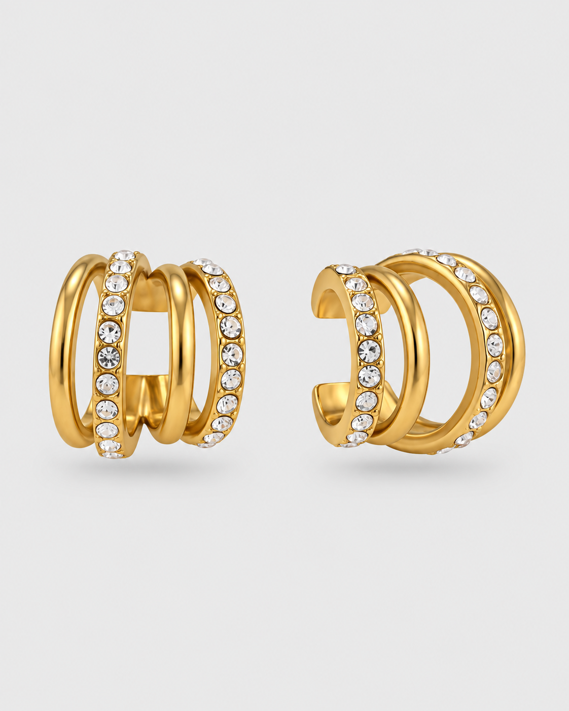 A pair of gold huggie hoop earrings with multiple stacked bands, some adorned with clear pavé-set round crystals, shown on a light gray background.