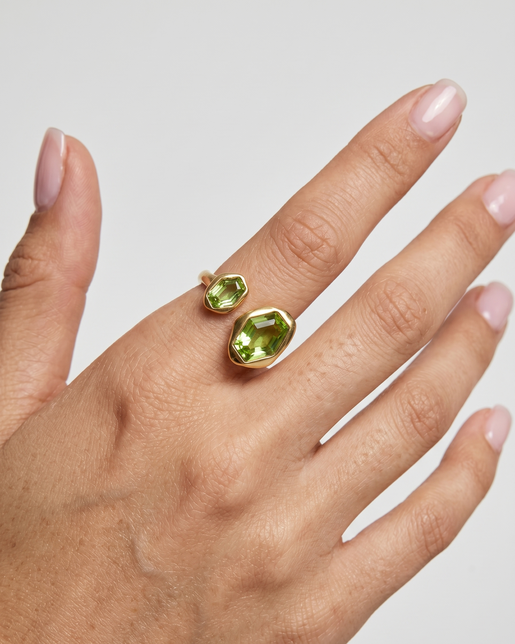 Hand wearing a gold ring with green gemstone on a neutral background