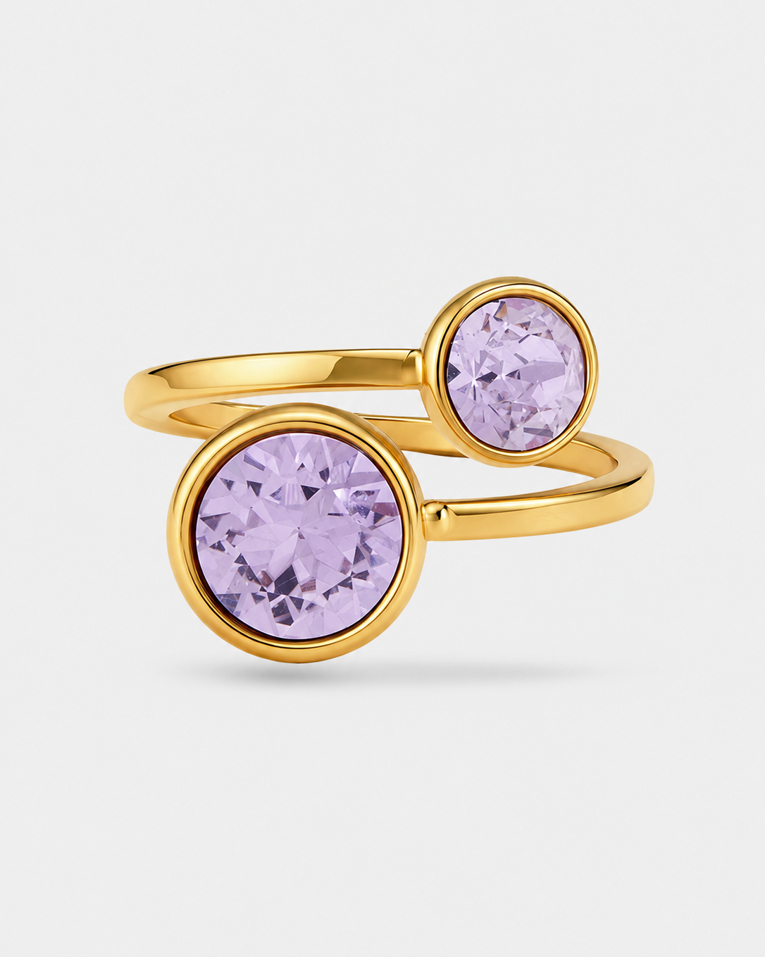 A gold-plated double-band ring featuring two bezel-set round light purple crystals, shown on a light gray background.