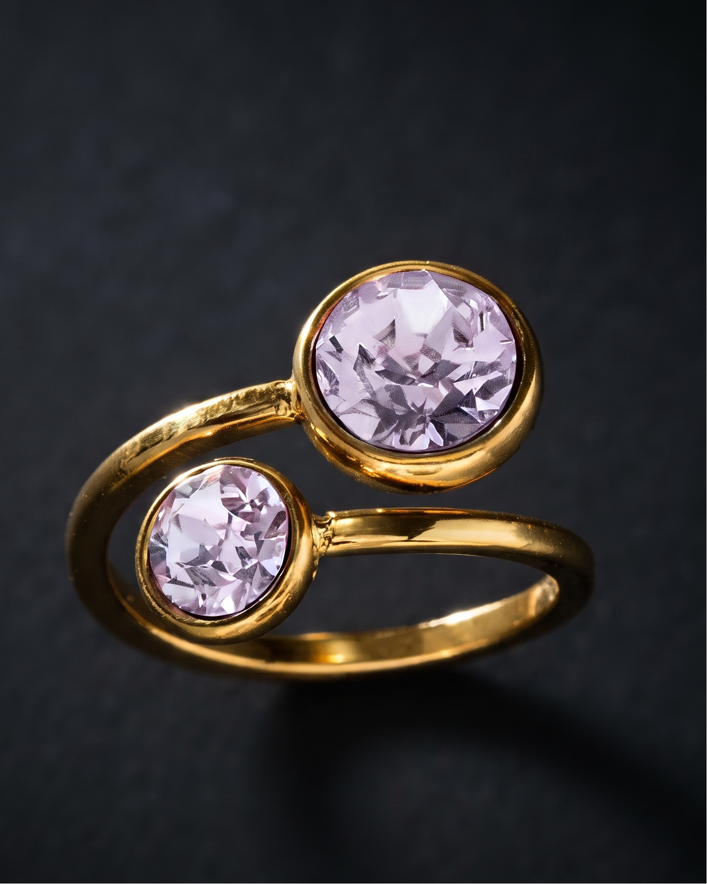 A gold ring with two round pale pink gemstones, photographed on a dark textured background.