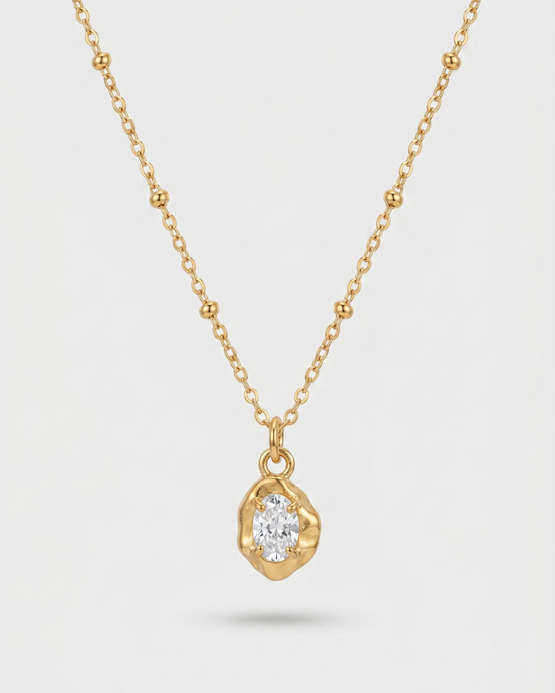 Gold necklace with a teardrop-shaped pendant on a light gray background
