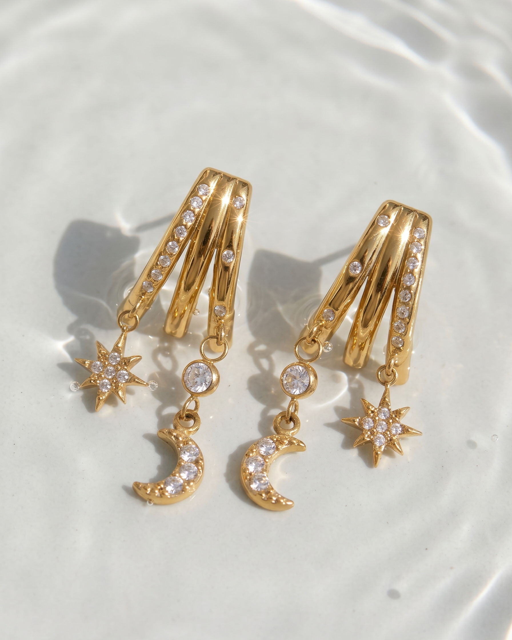 Gold hoop earrings with star and moon charms on a white plate