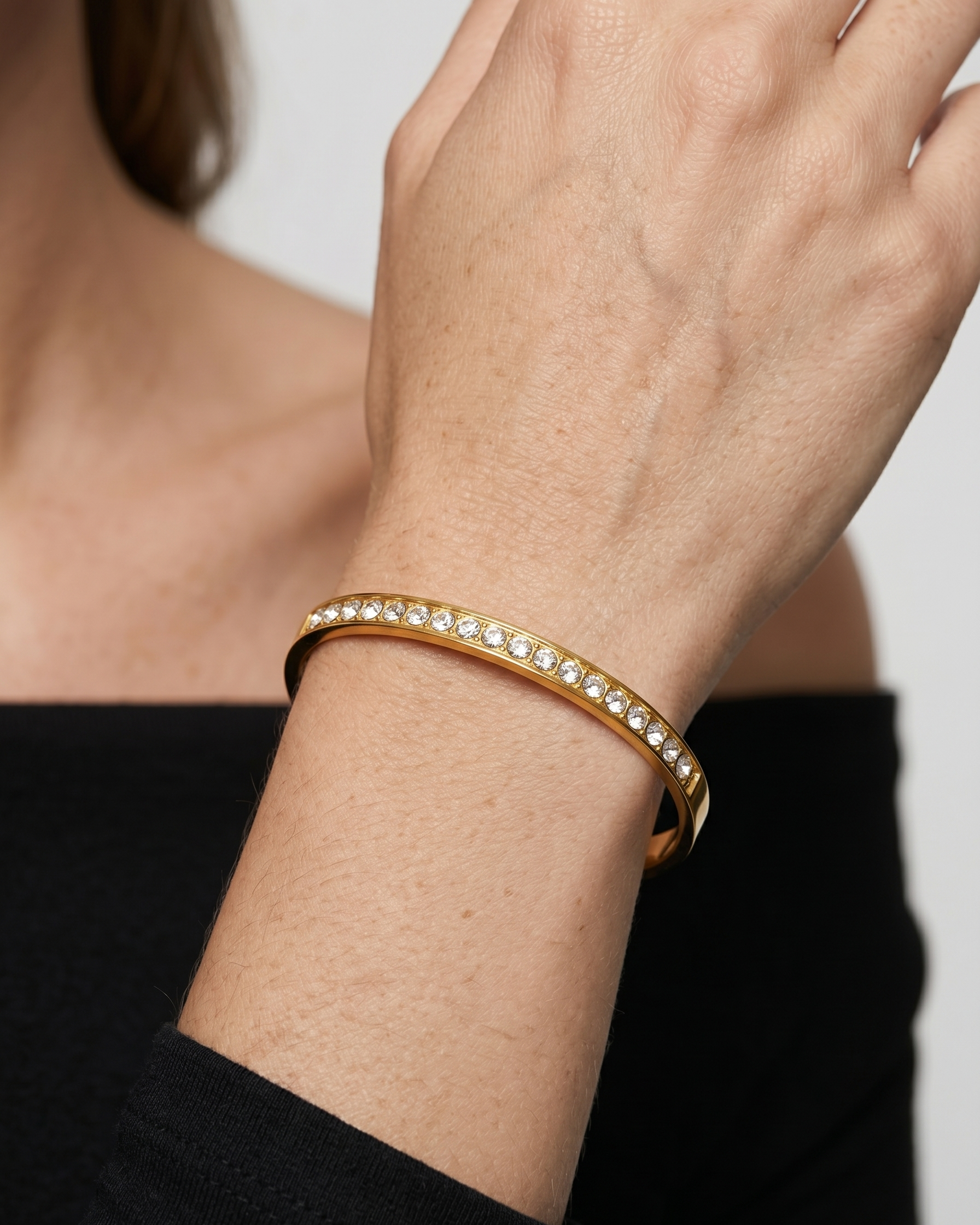 Gold bracelet with crystals on a wrist against a neutral background
