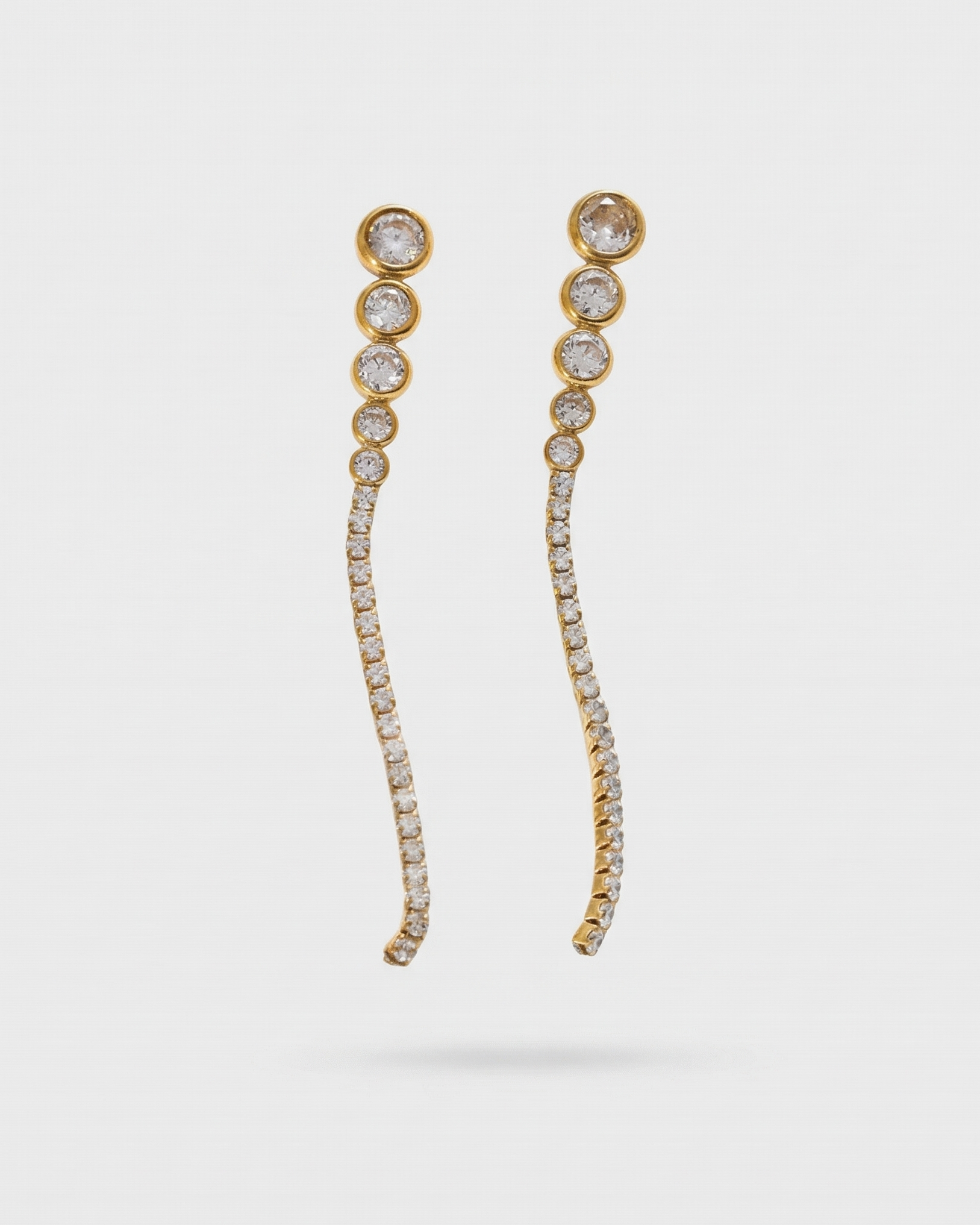 Gold earrings with clear stones on a light gray background