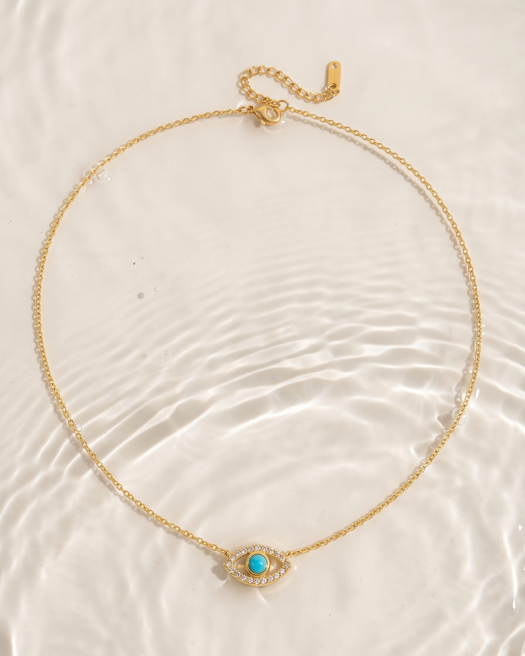 Gold necklace with a turquoise evil eye pendant on a textured white surface