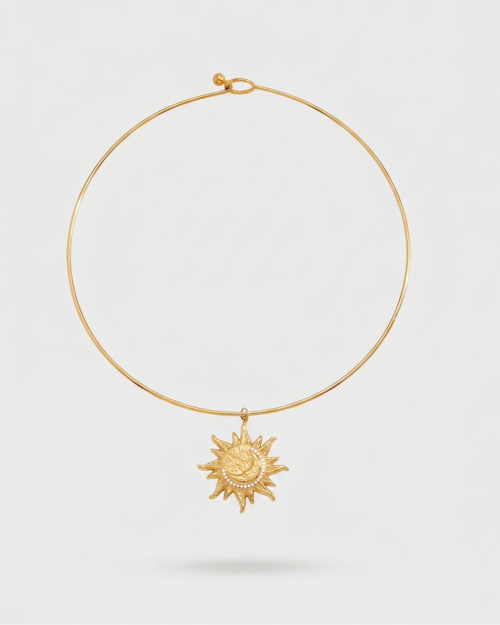 Gold necklace with a sun pendant on a light gray background