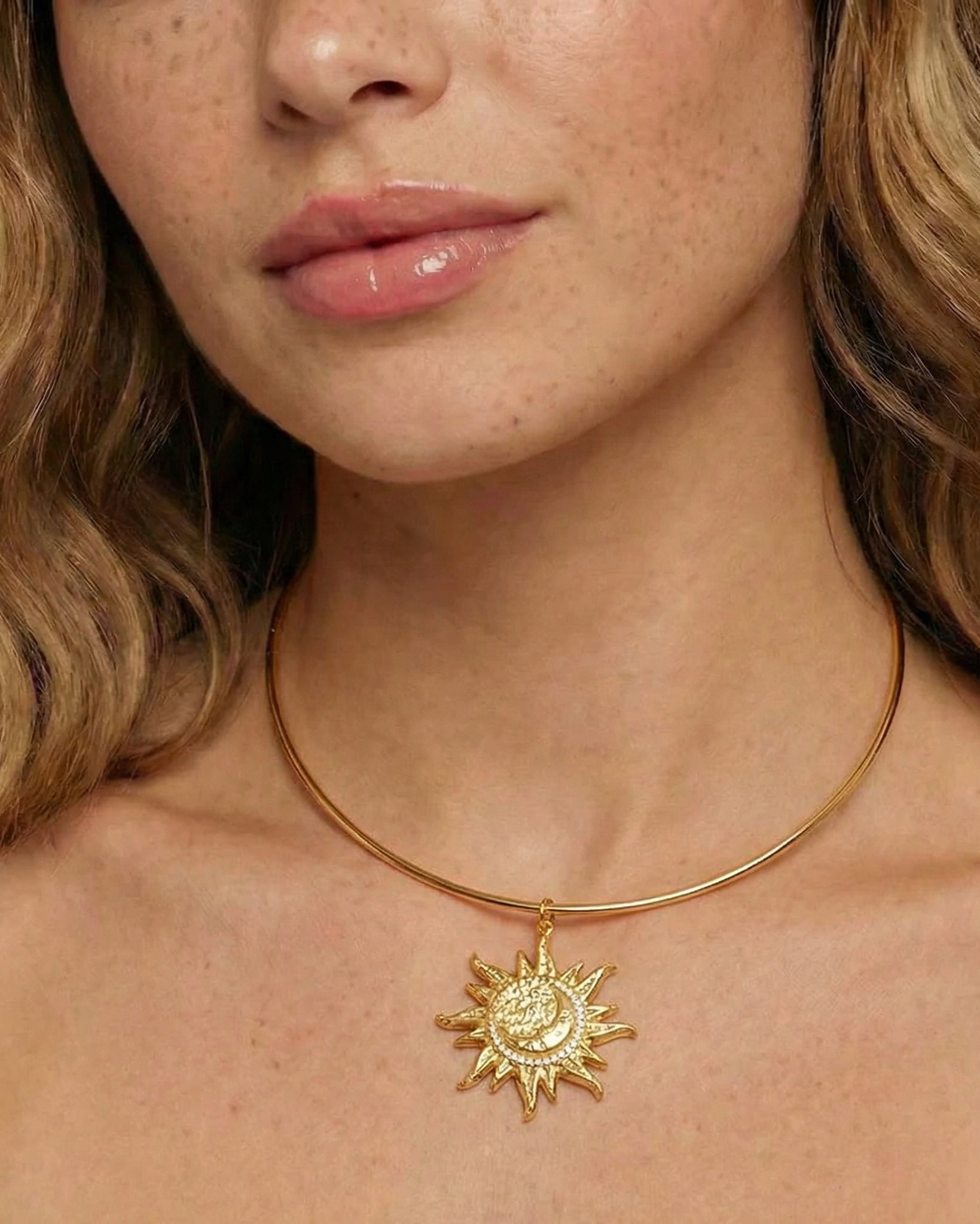 Close-up of a woman wearing a gold necklace with a sun pendant.