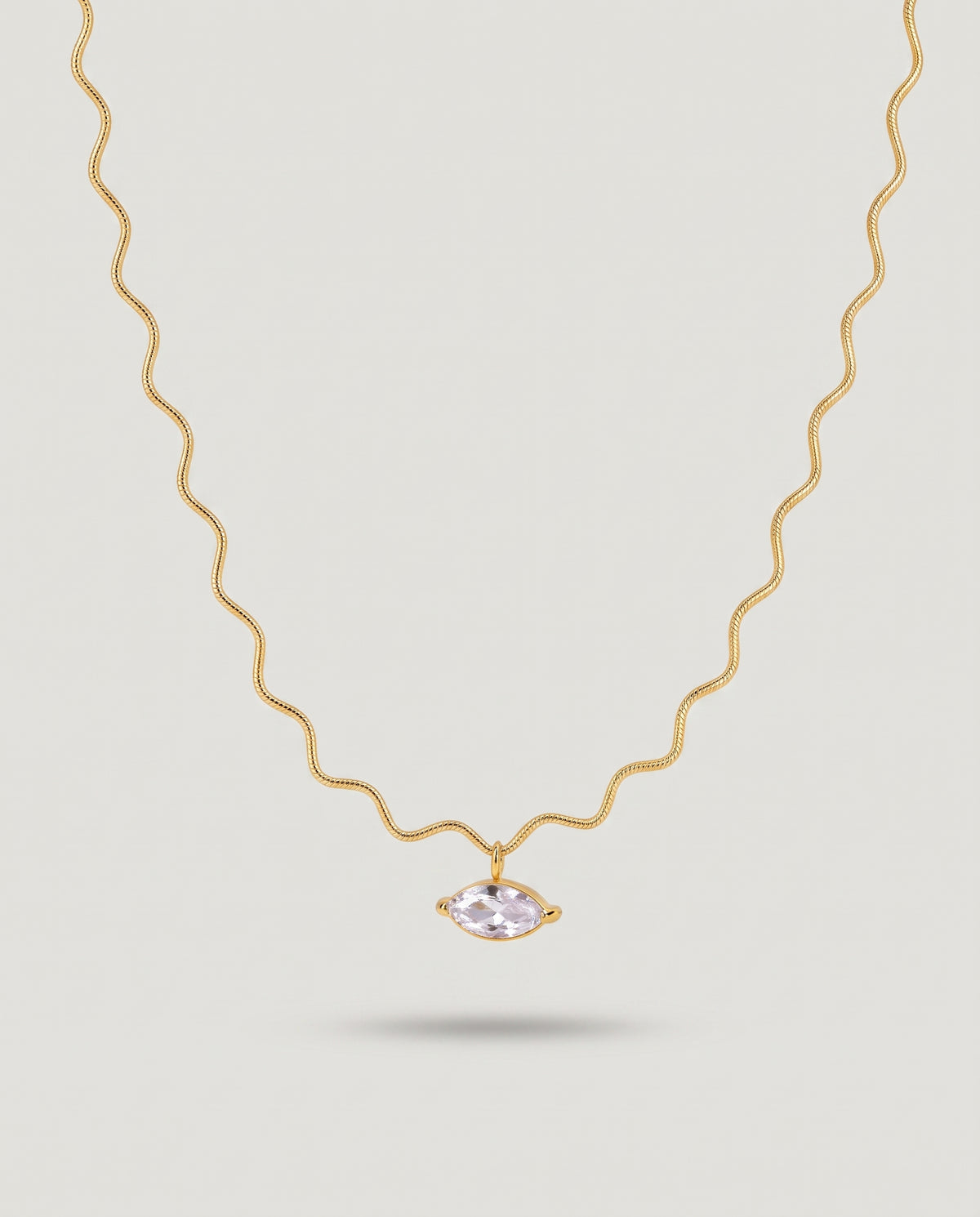 A delicate gold wavy chain necklace featuring a small marquise-cut pale pink gemstone pendant, displayed against a solid light gray background.